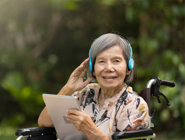 an old lady with Alzheimer's sitting on a wheelchair is wearing a headset and listening to the music